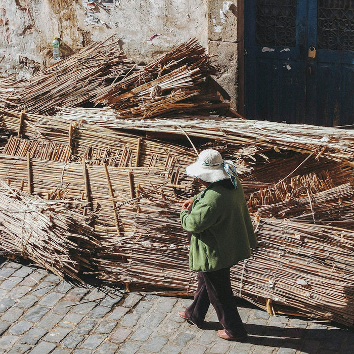person walking past brown wood pile on side of road