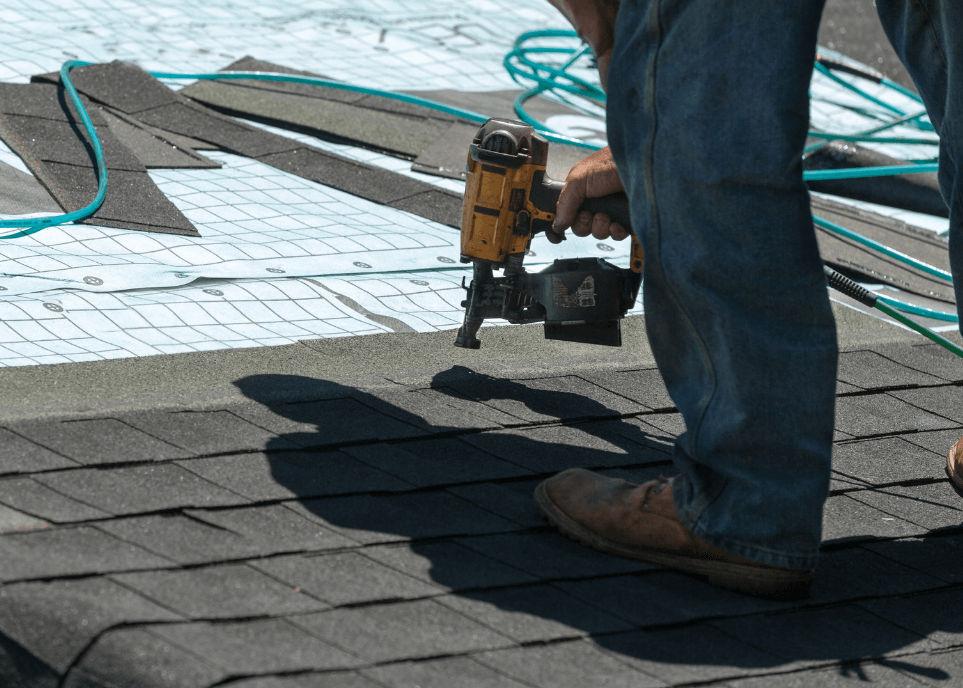 Worker fitting black bitumen roof shingles to a roof