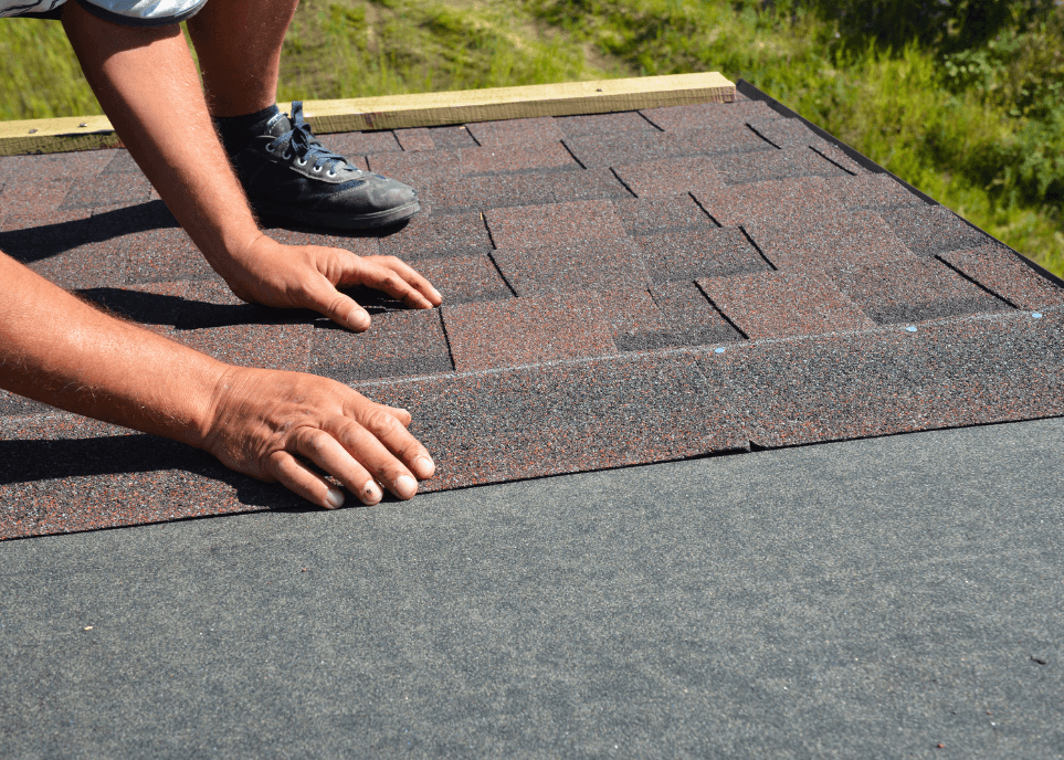 Worker fitting red bitumen roof shingles to a roof